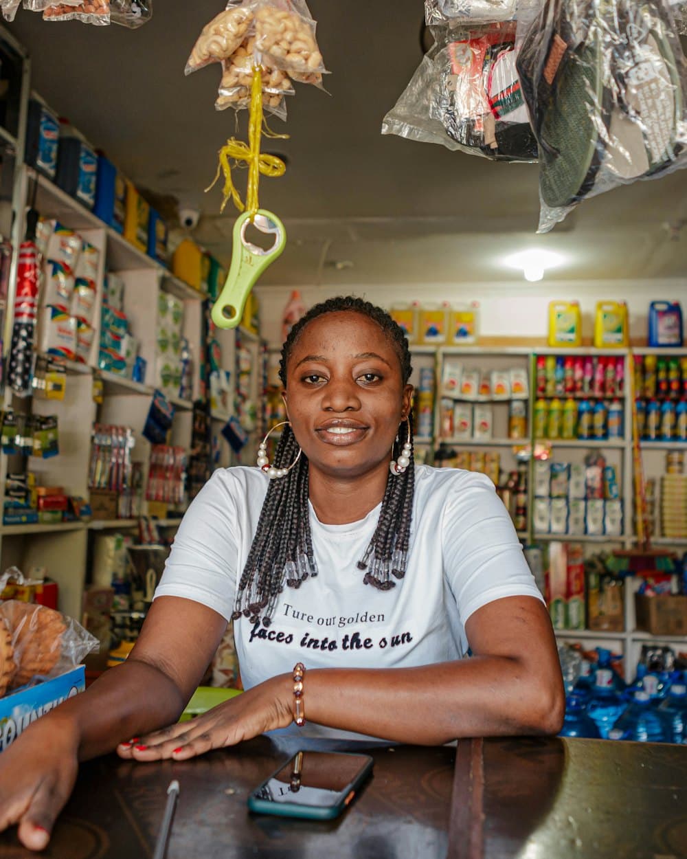 A shopkeeper behind her counter, her shelves stocked behind her